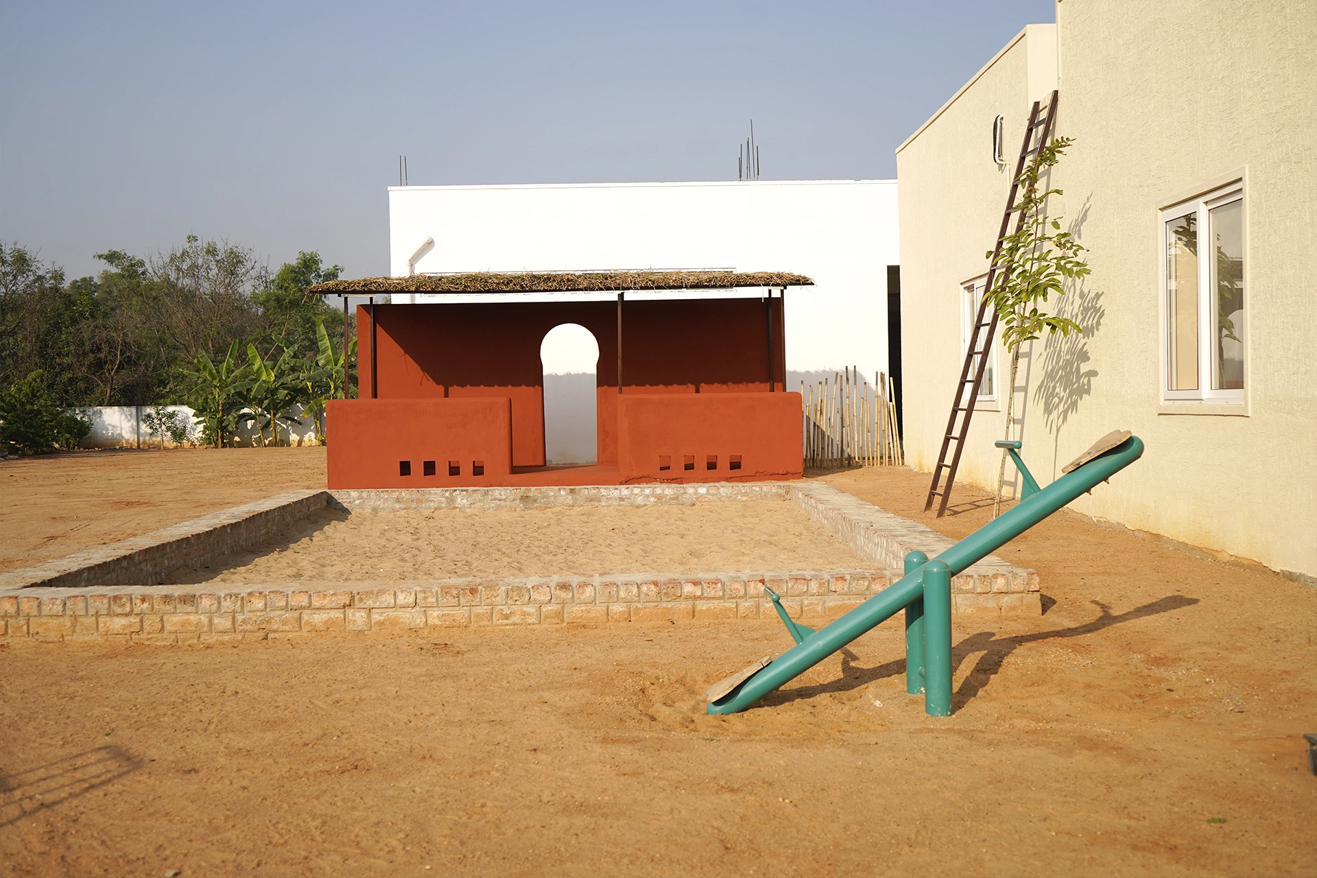 The terracotta play pavilion and seesaw on the sand