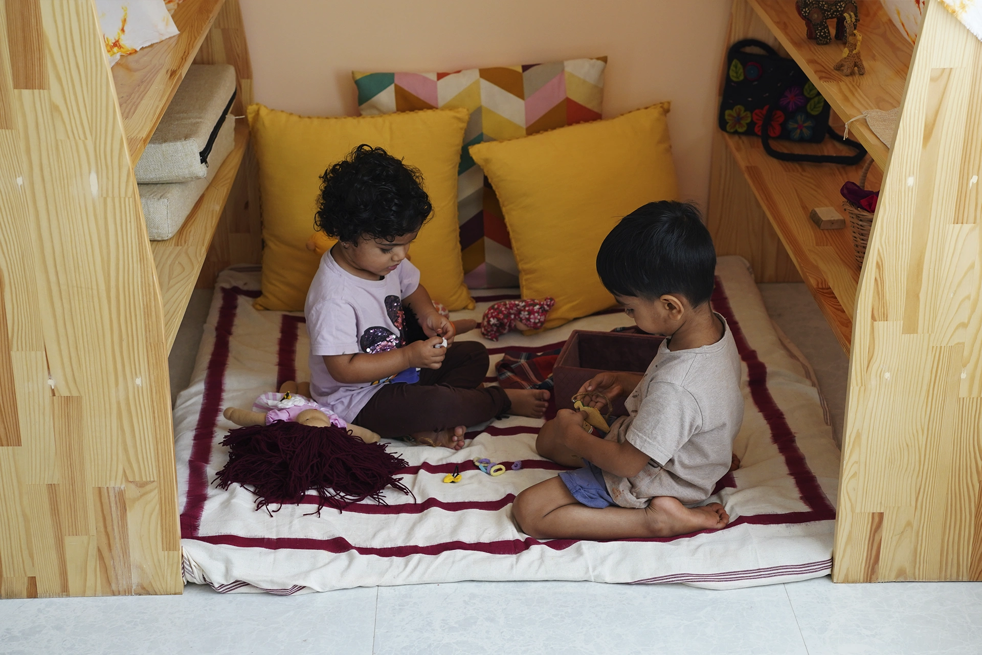 Two kindergarten children play with wooden toys among yellow cushions