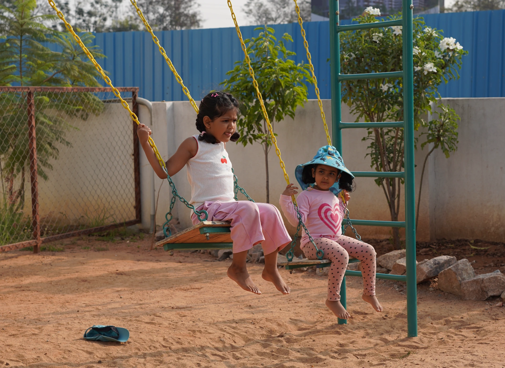 Two children on the swings under a tree in the Thraya playground
